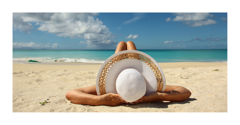 Women relaxing on beach with white hat on. 